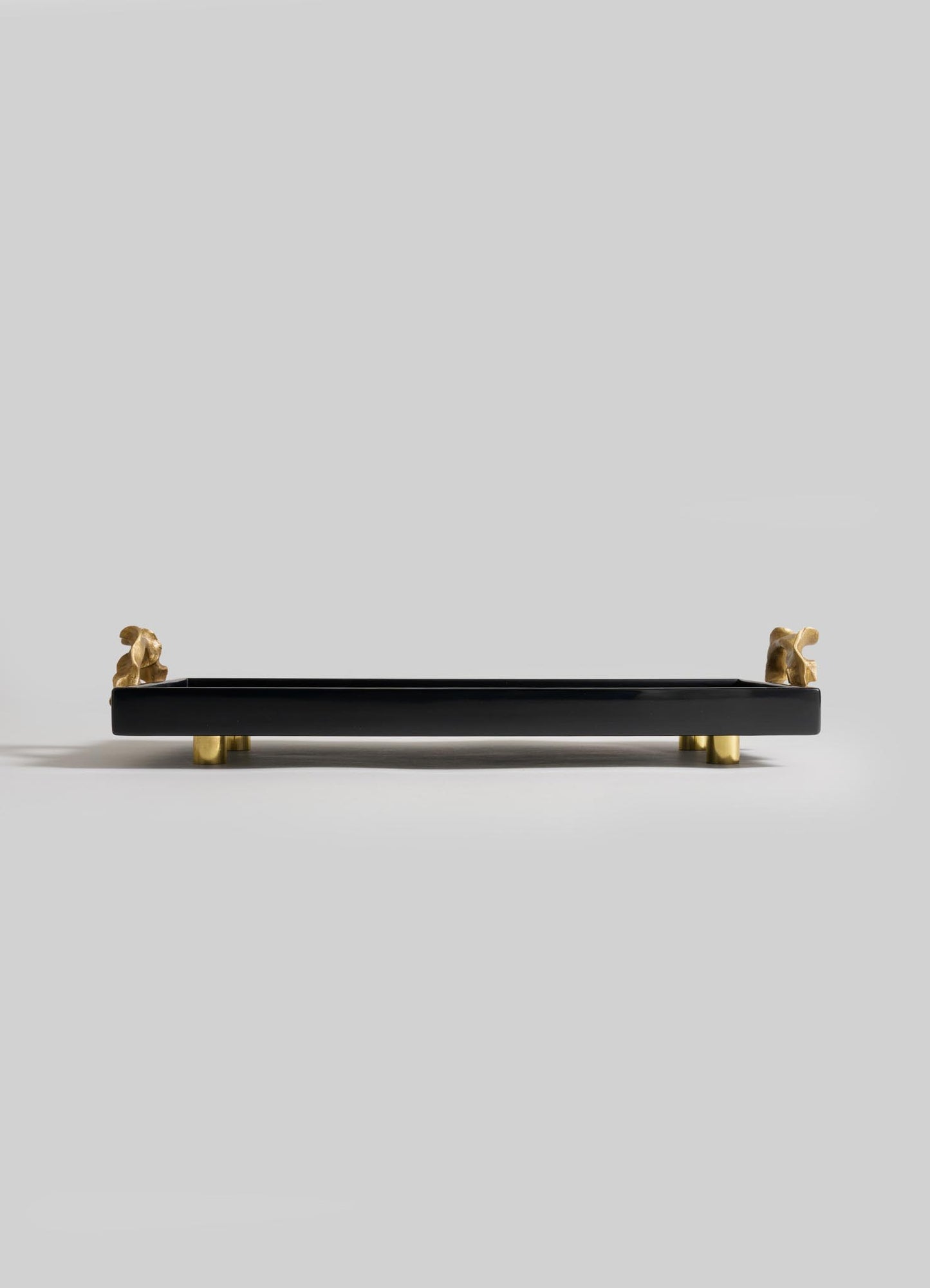 The VIYA Saffron Black Vanity Tray features a rectangular black design with four small gold dog figurines as legs and handles, evoking the elegance of saffron threads, set against a plain light gray background.