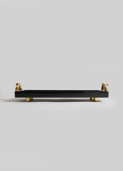 The VIYA Saffron Black Vanity Tray features a rectangular black design with four small gold dog figurines as legs and handles, evoking the elegance of saffron threads, set against a plain light gray background.