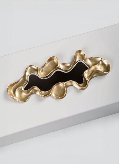The VIYA Saffron Tissue Box Large features a sculptural gold-toned design with wavy edges and a glossy black center, evoking contemporary elegance when displayed on a sleek white rectangular surface.