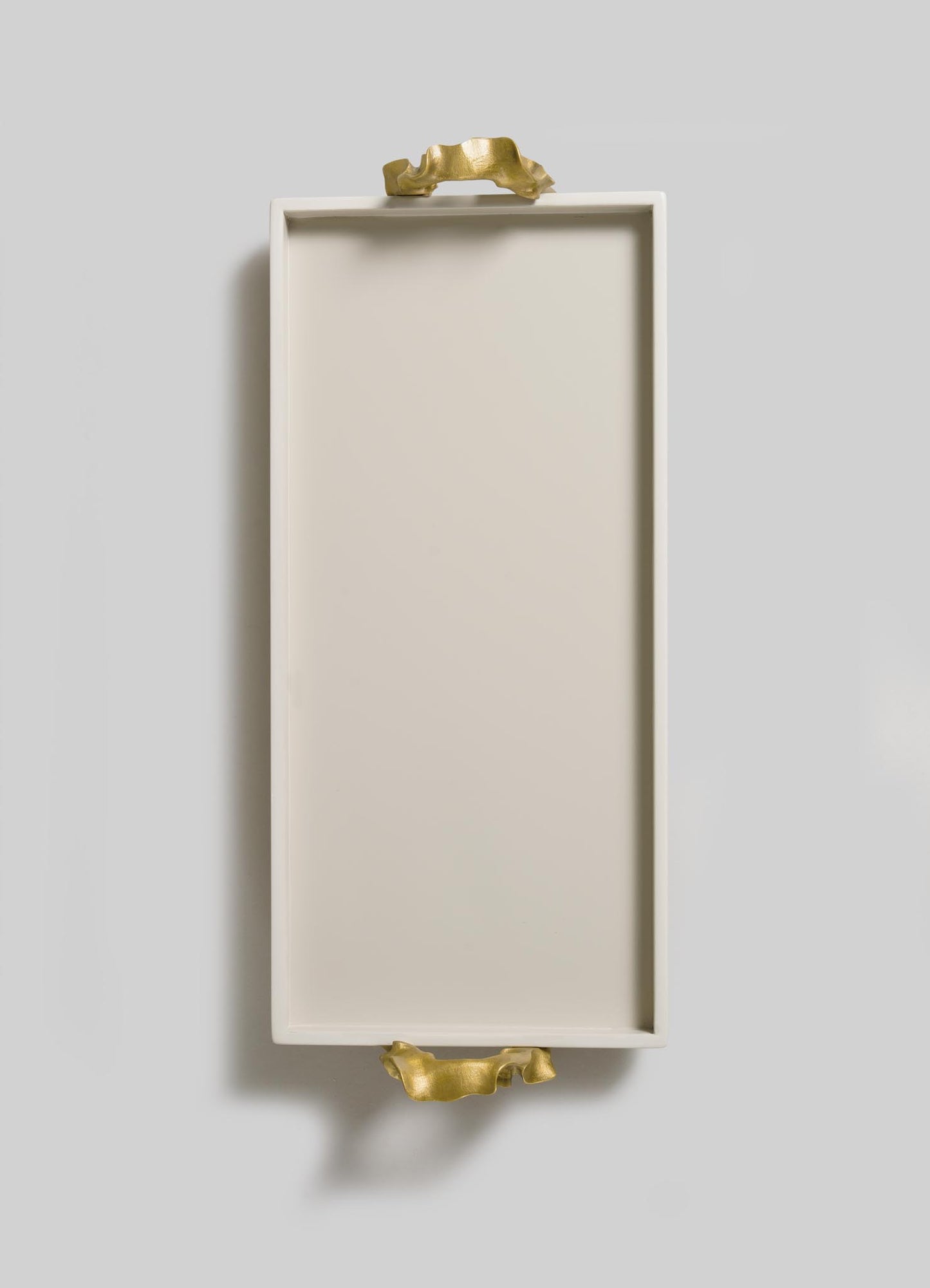 The Saffron Ecru Vanity Tray by VIYA features a rectangular white design with gold sculpted handles, inspired by contemporary bronzed objects, shown on a light grey background.