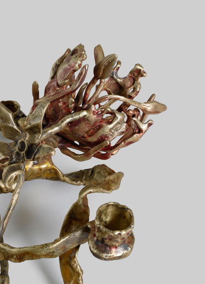 A sculptural art piece made of metal with a textured, organic form featuring intricate, openwork patterns in red, gold, and bronze tones. The design evokes natural motifs with a contemporary and artisanal style.