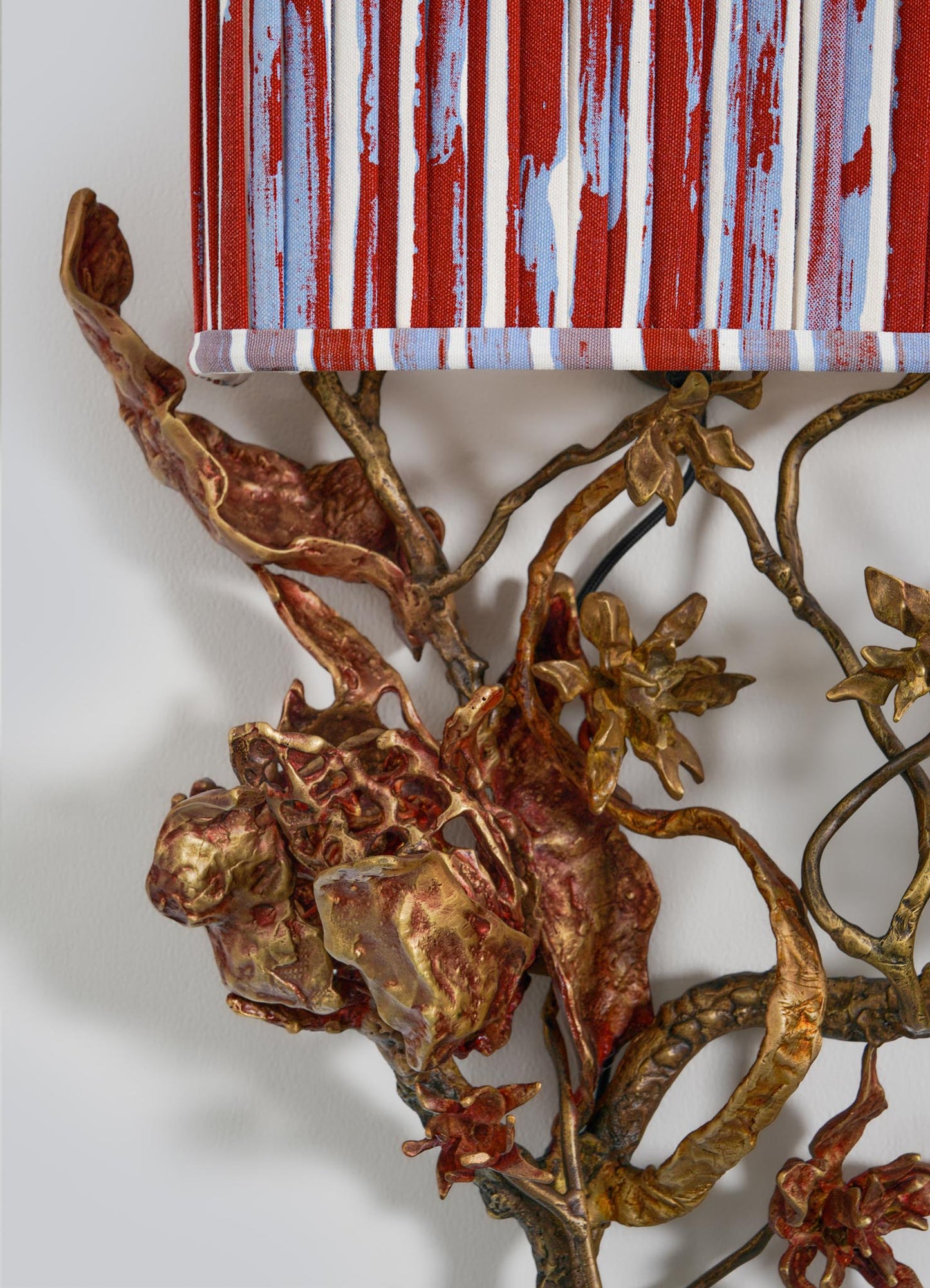 Close-up of VIYA’s Spring In Kashmir Wall Sconce A, featuring bronze-patina metal branches and leaves beneath a red, blue, and white striped painted surface—ideal for lovers of Kashmir-inspired home decor.