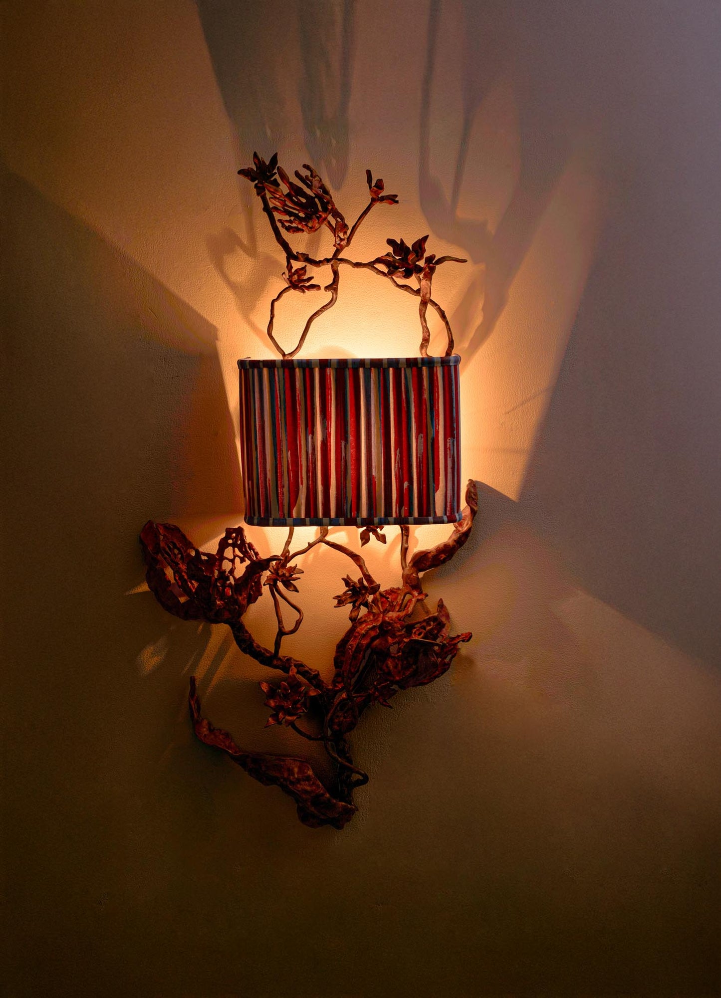 The VIYA Spring In Kashmir Wall Sconce B features a striped lampshade and metal branches in brass and bronze tones, casting warm light and artistic shadows for an elegant touch inspired by Kashmir.