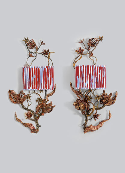 The VIYA "Spring In Kashmir Wall Sconce B" is a vertical home decor piece featuring red and white striped rectangular boxes with brass and bronze branching vines, inspired by Kashmir artistry, set against a plain gray background.