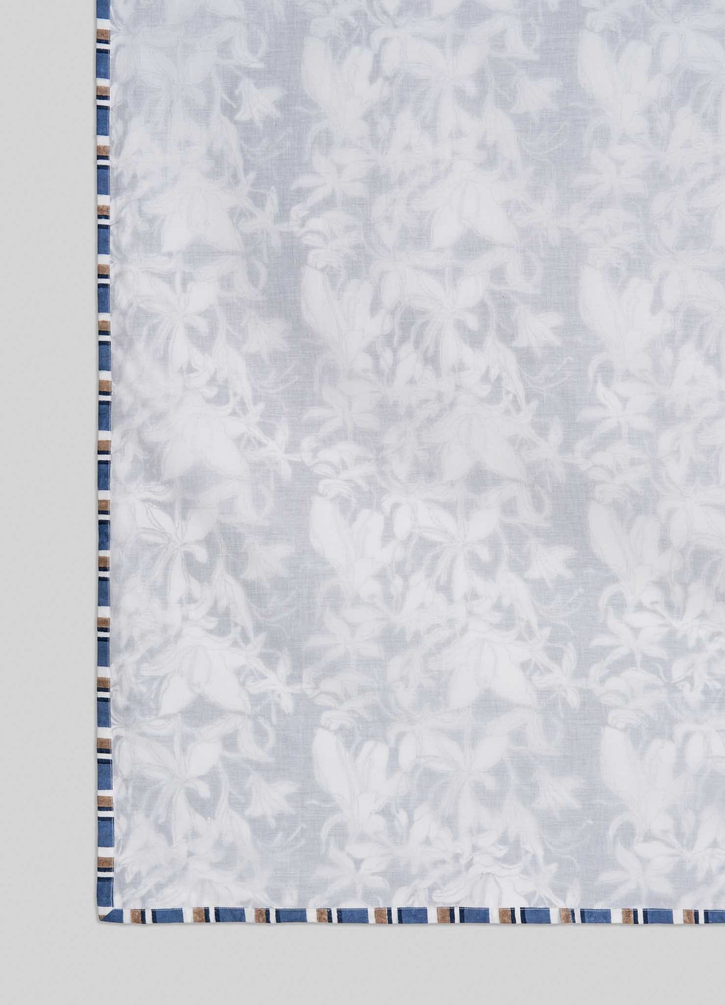 The Viya Spring Bouquet Blue Single Dohar features sheer white fabric with a subtle floral design inspired by Indian gardens and a border of alternating blue, tan, and white stripes, shown against a light gray background.