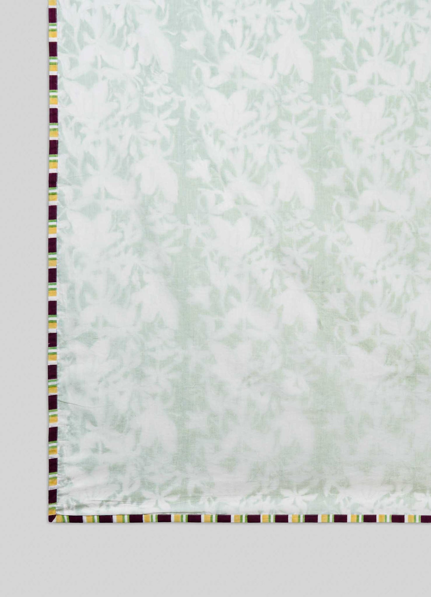 The Viya Spring Bouquet Green King Size Dohar features a light, semi-transparent white fabric with a subtle floral pattern inspired by Indian garden bedding and a border of alternating yellow, maroon, and white rectangular blocks.