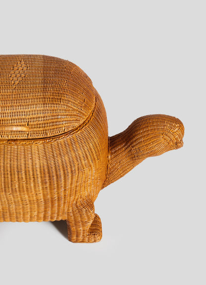 The VIYA Tortoise Laundry Basket features cane weaving in a natural color, shaped like a tortoise with an oval shell, one leg, and a long neck with head, all set against a plain light gray background.