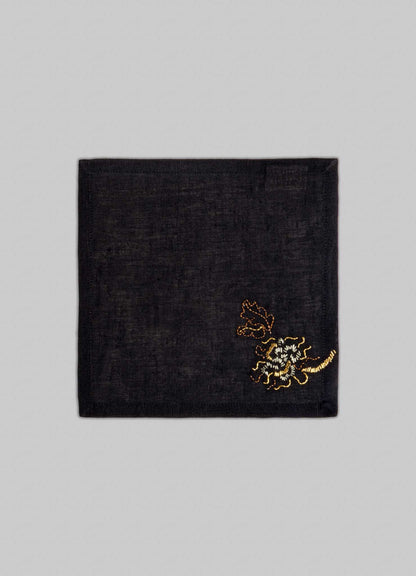 The Viya Tree Full of Parrots Hand Embroidered Black & Gold Cocktail Napkins—set of 4—feature a gold and brown floral design on black linen, shown against a light gray background.
