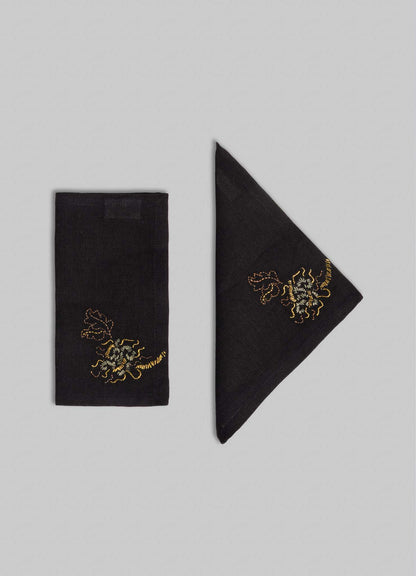 Set of four black and gold "Tree Full of Parrots" hand-embroidered cocktail napkins by Viya, shown folded in various styles with intricate parrot designs, displayed on a light gray background.