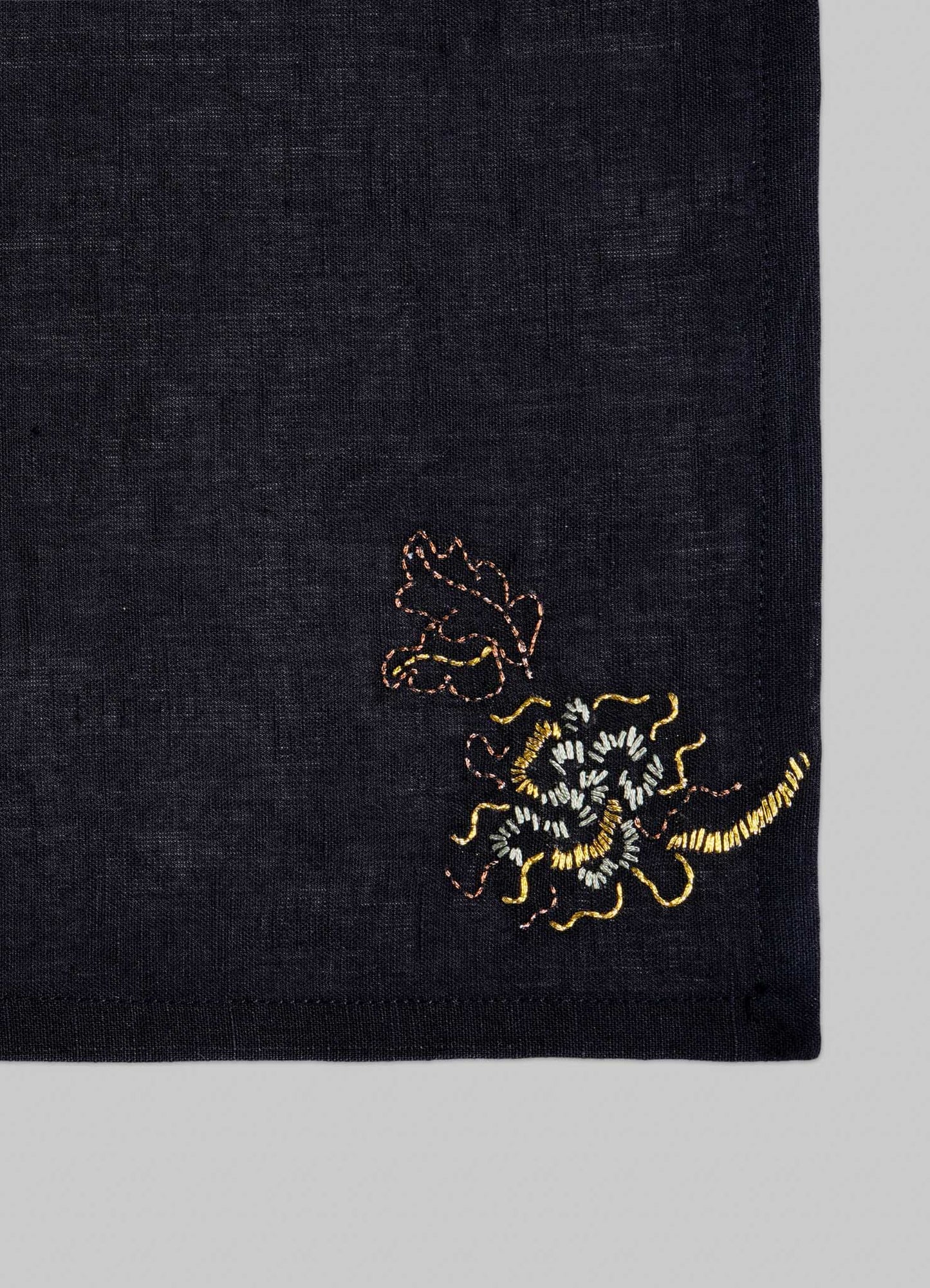 The Viya Tree Full of Parrots Hand Embroidered Black & Gold Cocktail Napkins (Set of 4) feature dark linen with small yellow and brown floral embroidery in one corner, set against a plain light grey background.