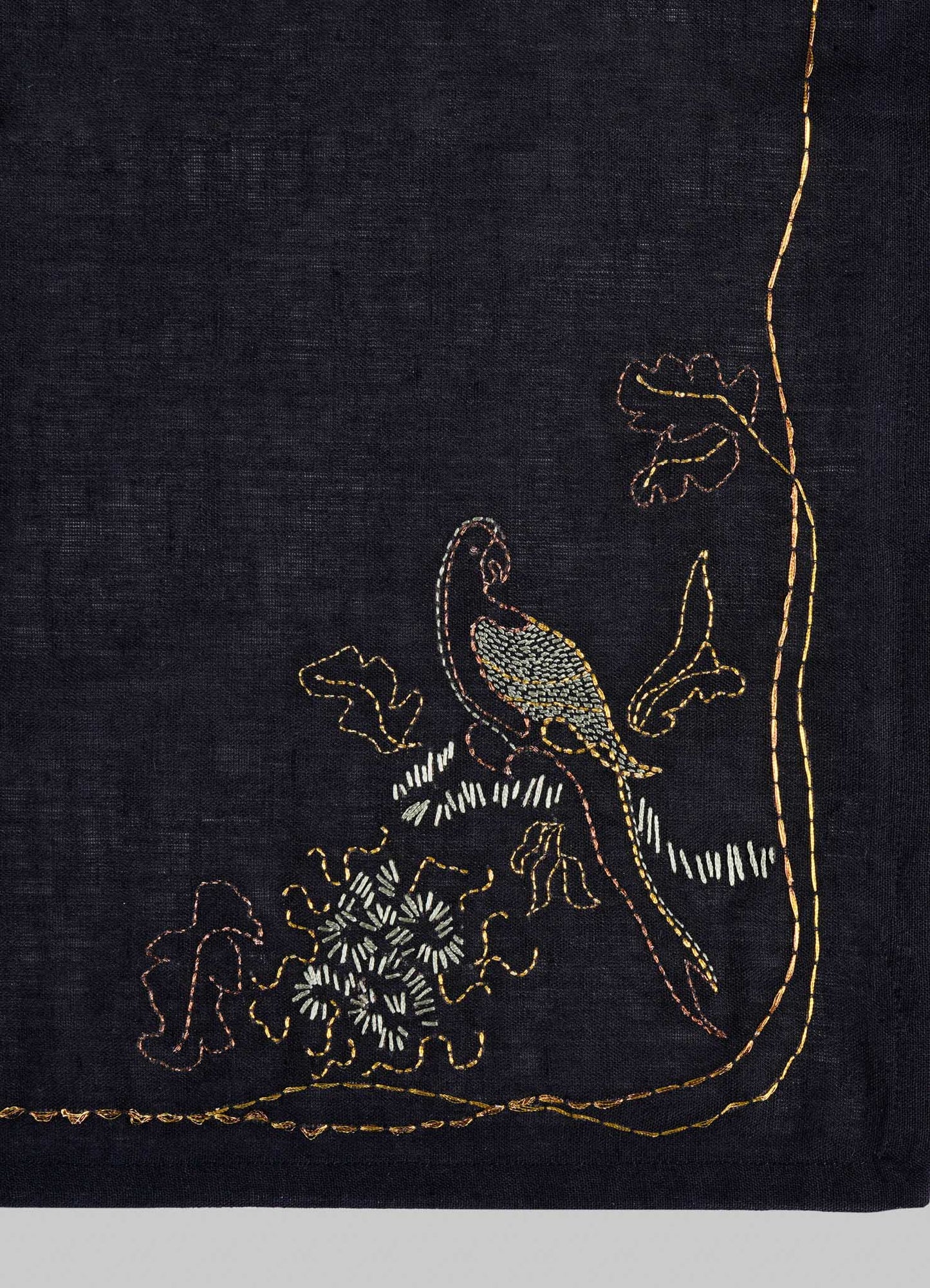 The Viya Tree Full of Parrots Hand Embroidered Black & Gold Napkin features a vibrant parrot on a leafy branch in yellow, brown, white, and green threads—an elegant table linen that symbolizes blessings and good fortune.