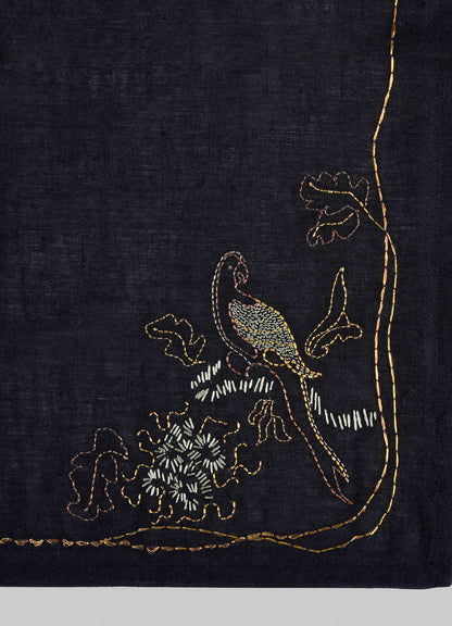 The Viya Tree Full of Parrots Hand Embroidered Black & Gold Napkin features a vibrant parrot on a leafy branch in yellow, brown, white, and green threads—an elegant table linen that symbolizes blessings and good fortune.