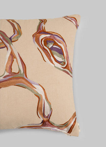 The Viya Tutti Frutti Salmon Pink Cushion Cover (18"x18") features abstract wavy embroidery in brown, orange, purple, and white on a light gray background with a small fabric tag in the bottom right corner.