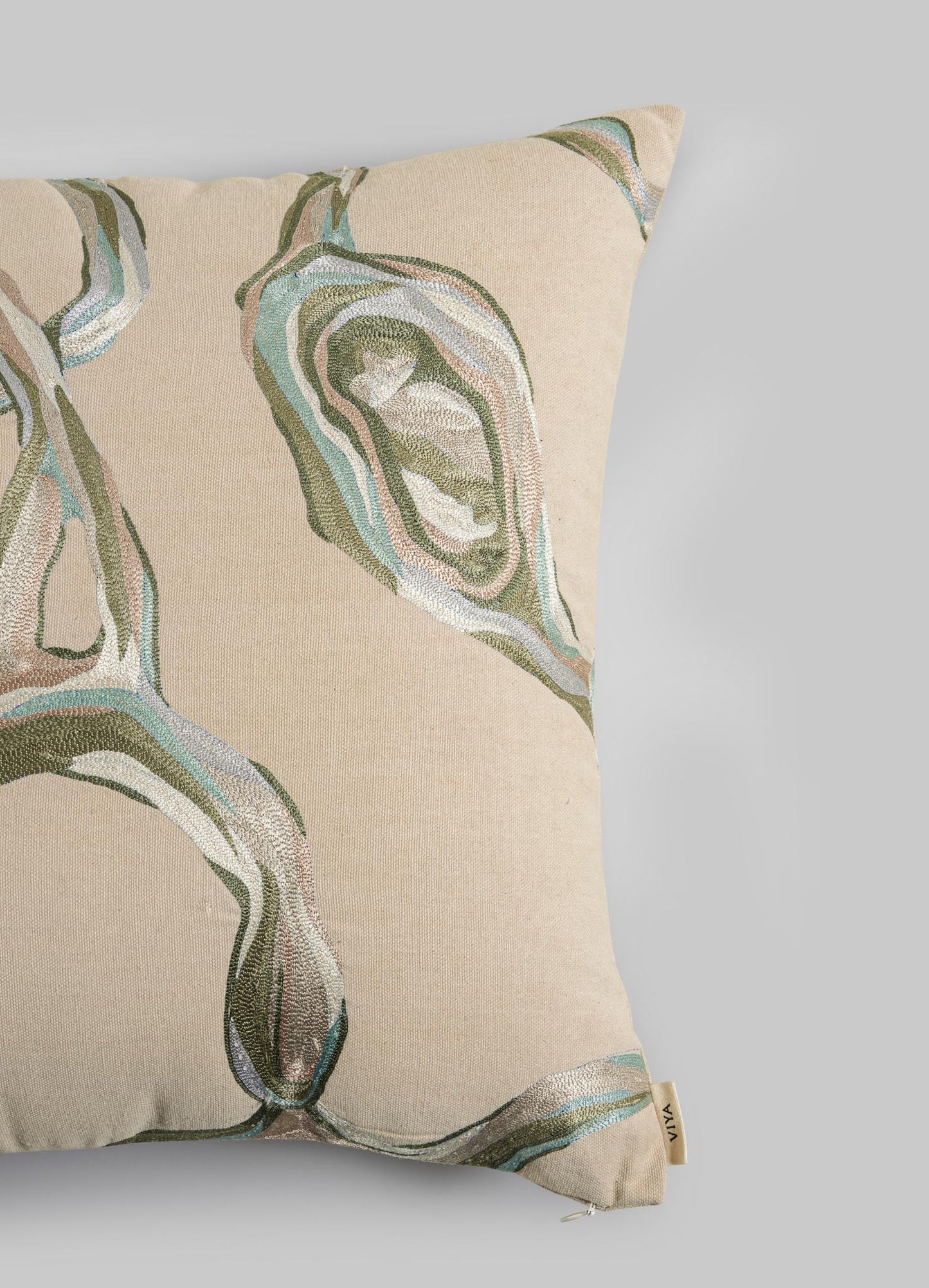 The Viya Tutti Frutti Sea Green Cushion Cover 18"x18" features an abstract green, blue, and brown pattern on beige, a small beige fabric tag in the corner, and is styled against a plain light gray background.