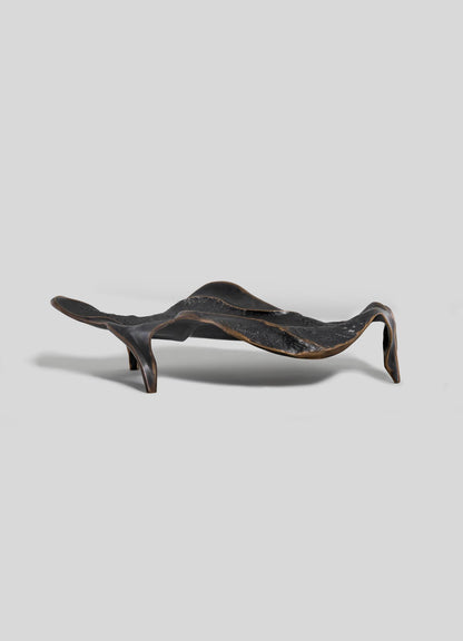 The VIYA Under The Banyan Bowl Large is a sculptural bronze piece with an organic, wavy shape and three asymmetrical legs, inspired by the banyan tree's longevity and shown against a plain light gray background.